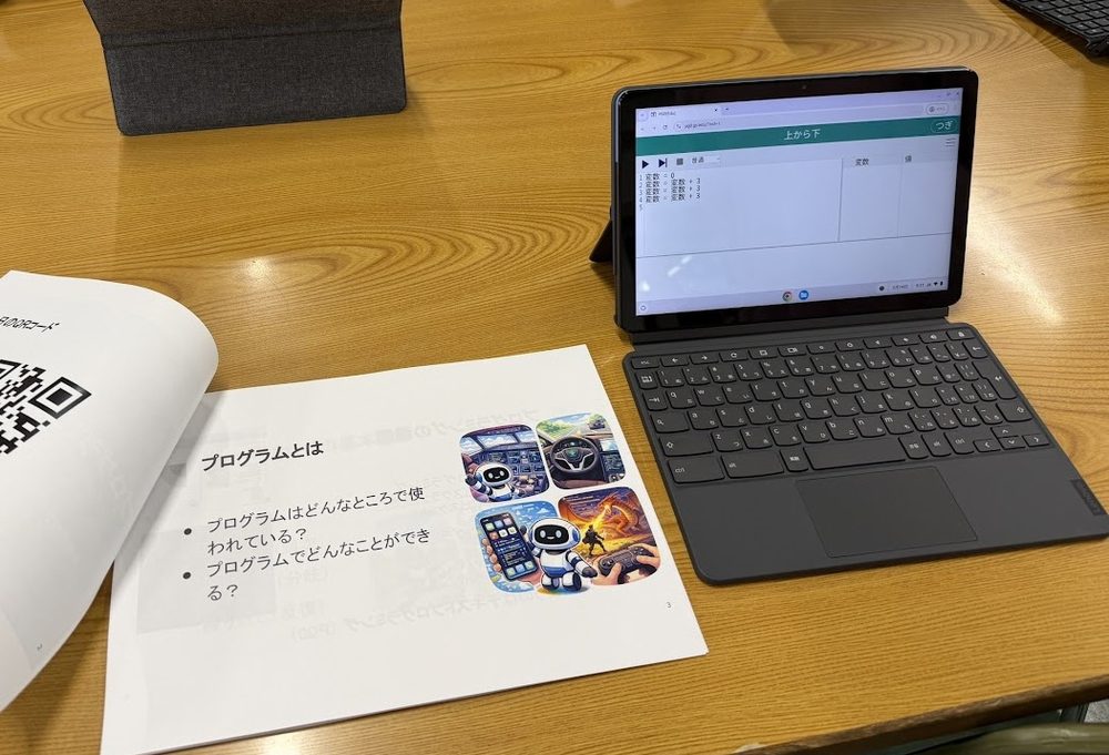 机の上のタブレットPCでPG0を開き、配布資料を見ながらプログラムを書いている様子
